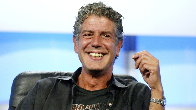 Anthony Bourdain smiling with hand raised