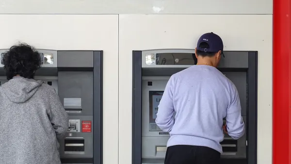 Two people use side-by-side ATMs.