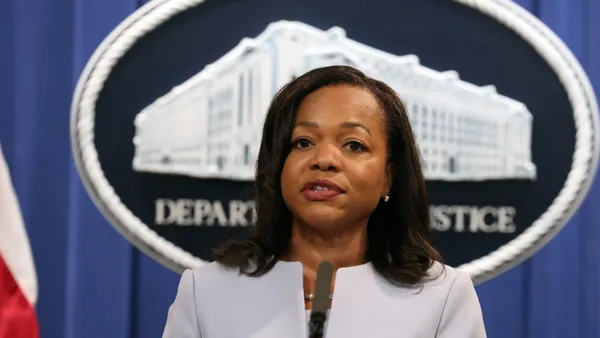 Kristen Clarke speaks at a podium in front of a curtain backdrop and a DOJ logo