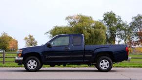 Profile view of a GMC Canyon compact pickup truck parked in front of a fence and trees.