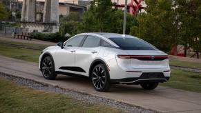 A rear side profile shot of a 2023 Toyota Crown Platinum lift-up sedan model in Oxygen White in a park. Toyota Crown sales have performed not amazingly so far.