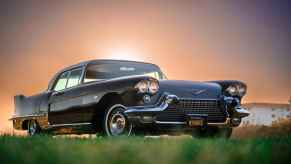 A black 1958 Cadillac Eldorado Brougham parked on grass in right front angle view with sun barely peeking over roofline