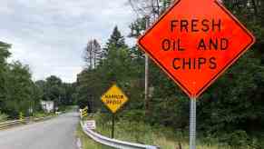 Bright orange "Fresh Oil and Chips" construction sign on a refinished country road.