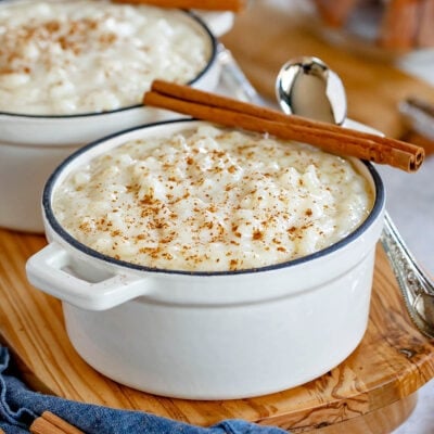 rice pudding served in 2 small white cast iron pots with cinnamon sticks resting on the rim.