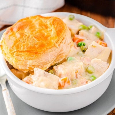 bowl filled with turkey pot pie and topped with a biscuit. the rest of the pot pie can be seen in the cast iron skillet in the background.