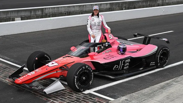 Professional race car driver Katherine Legge is seen standing on a race track next to an E.l.f. Cosmetics-branded car while also wearing E.l.f.-branded gear for the Indy 500.