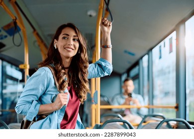 Young smiling woman holding onto a handle while traveling by public bus. Stock Photo
