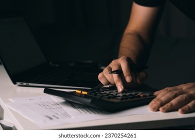 Asian man is using a calculator to calculate his family's monthly miscellaneous expenses at his home. Stock Photo