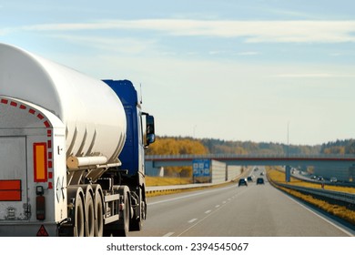 Dangerous goods transportation by semi truck with propane tank. The tank truck has a side view and shows hazard labels for high-temperature liquid and miscellaneous hazards. The truck follows the ADR Stock Photo