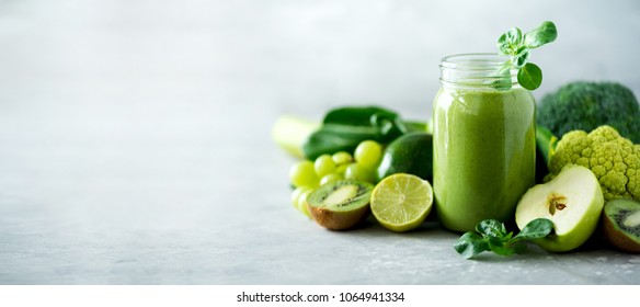 Glass jar mugs with green health smoothie, kale leaves, lime, apple, kiwi, grapes, banana, avocado, lettuce. Copy space. Raw, vegan, vegetarian, alkaline food concept. Banner. Stock Photo
