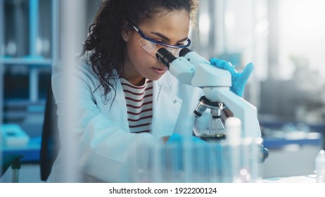 Medical Science Laboratory: Portrait of Beautiful Black Scientist Looking Under Microscope Does Analysis of Test Sample. Ambitious Young Biotechnology Specialist, working with Advanced Equipment Stock Photo