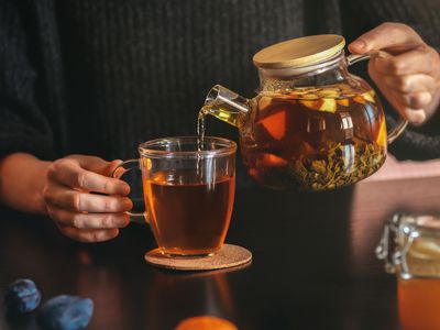Female hand pouring tea into transparent cup.