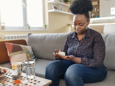 Black female taking medication at her home in the living room