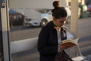 Woman sitting on a bench in a public space, reading book.