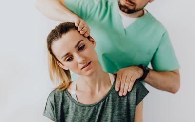 A young white woman getting an adjustment to her neck by an unseen male healthcare professional in light green scrubs.