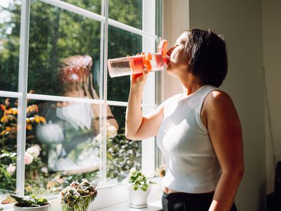 A person drinking water from a water bottle while looking out a window