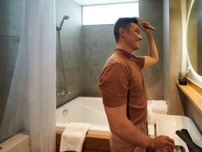 An Asian man happily brushing his hair in front of the mirror. 