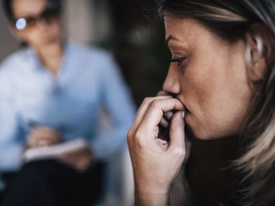 Woman with anxiety disorder, biting fingernails, talking to mental health professional