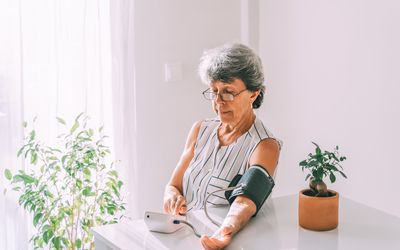 Woman seated in a relaxed position with arm supported, measuring her blood pressure at home. 