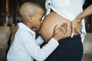 Image of young child embracing pregnant person's pregnant belly.