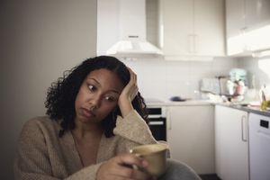 Young woman sitting in a kitchen while holding a mug, looking to the side appearing pensive