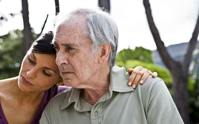 adult woman resting head on senior father's shoulder