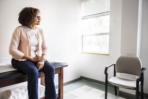Woman sitting on exam table in doctors' office, looking out the window.