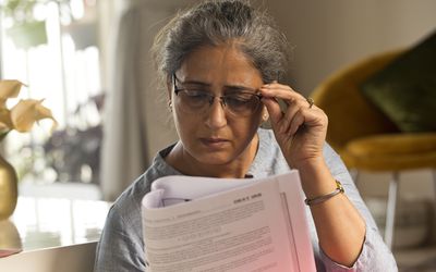 An older adult holding their eyeglasses trying to read a piece of paper, they might be struggling to see due to having geographic atrophy.