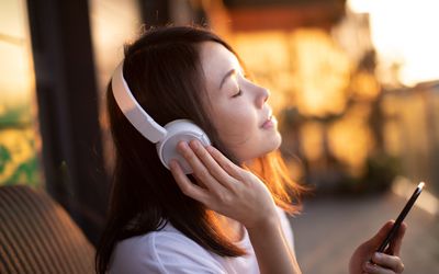 Young Woman Enjoying Music Over Headphones And Using Smart Phone