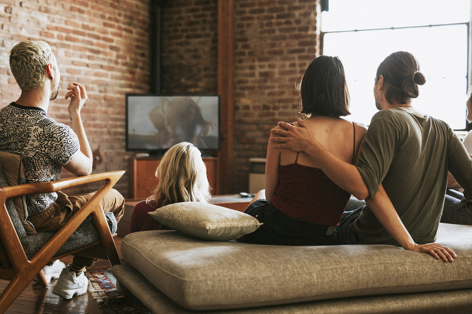 Group of young adults watch TV together in an apartment 