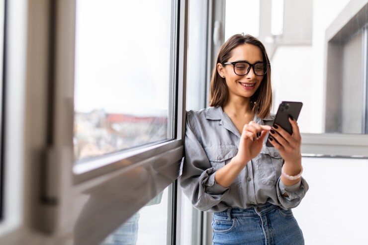 Woman standing in front of a window texting on her phone 