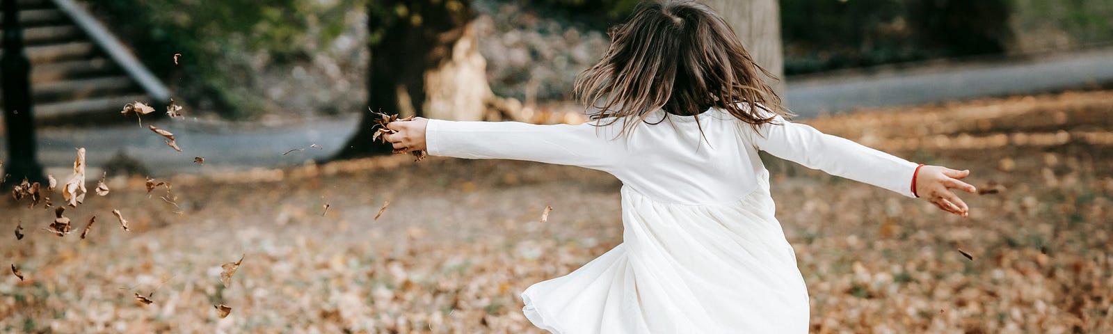Little girl with her arms outstretched dancing around in the fall leaves