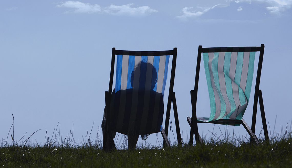 The silhouette of a woman sitting in a lawn chair next to a second empty lawn chair