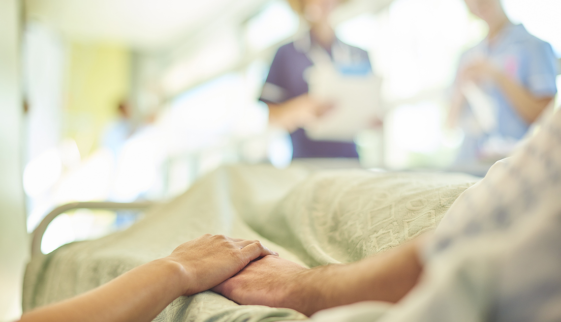 close up of a woman holding the hand of her dad who is in a hospital bed