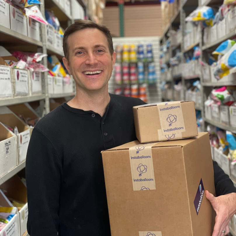 Jason Handman, CEO of instaballoons Wholesale, standing in a shipping room holding two boxes