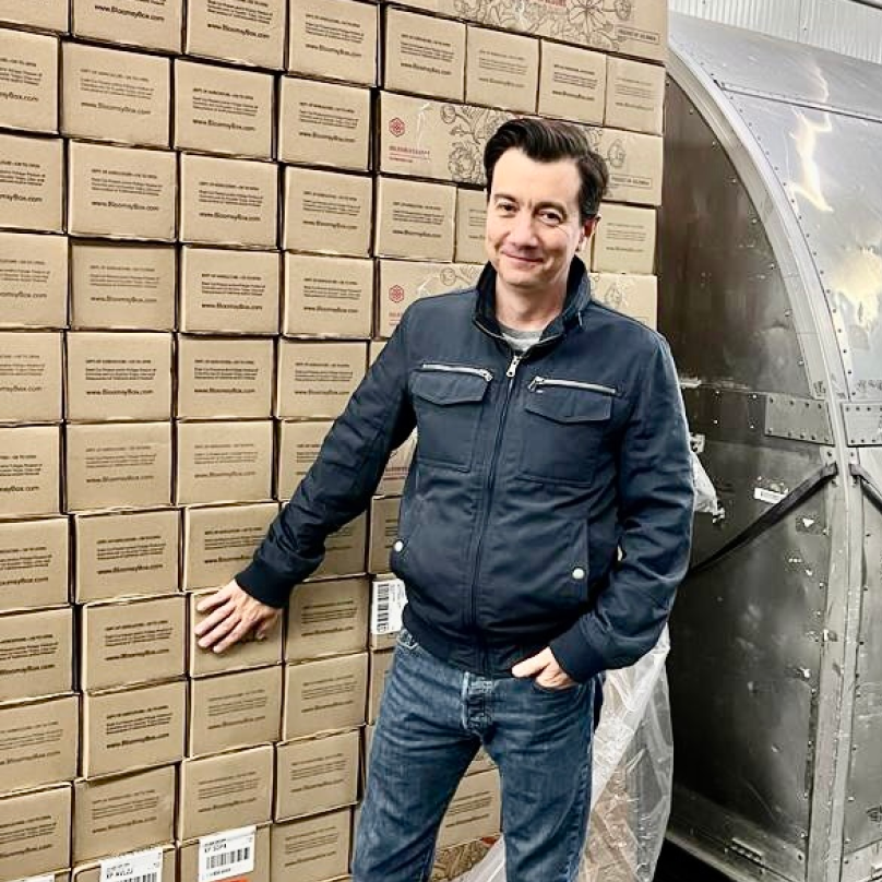 Man looking at the camera while standing beside a large stack of cardboard boxes
