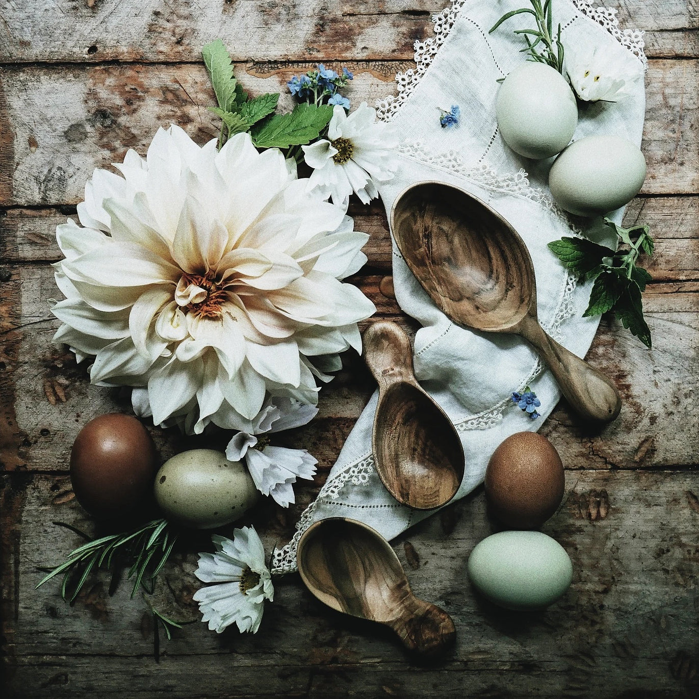 Wooden spoons are arranged on a table with eggs and flowers