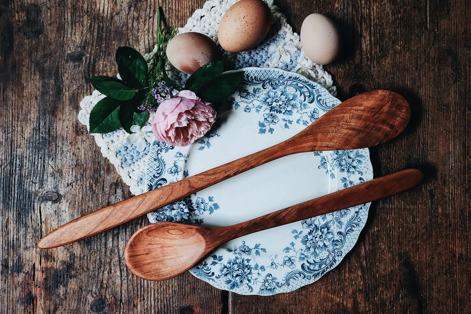 Handmade wooden spoons are arranged on a fancy plate and surrounded by eggs and flowers