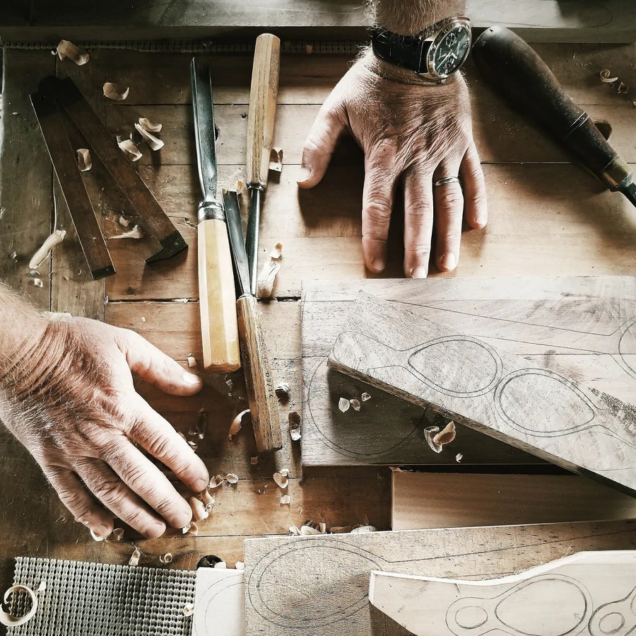 Hands reach into the frame where a work table is cluttered with woodworking tools