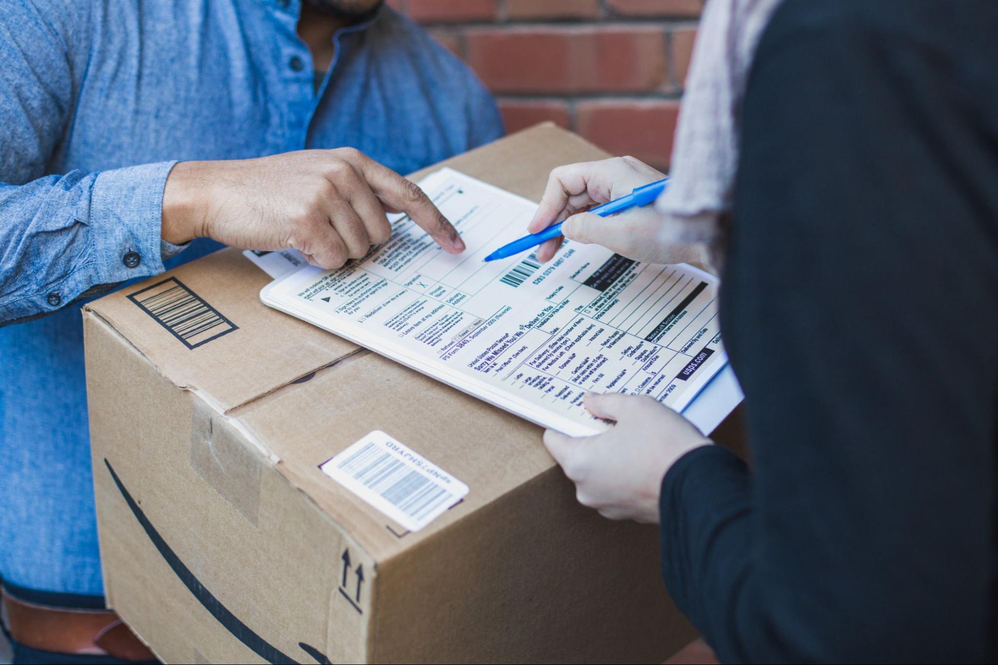 A person holding an Amazon package, directing another person to sign a packing slip