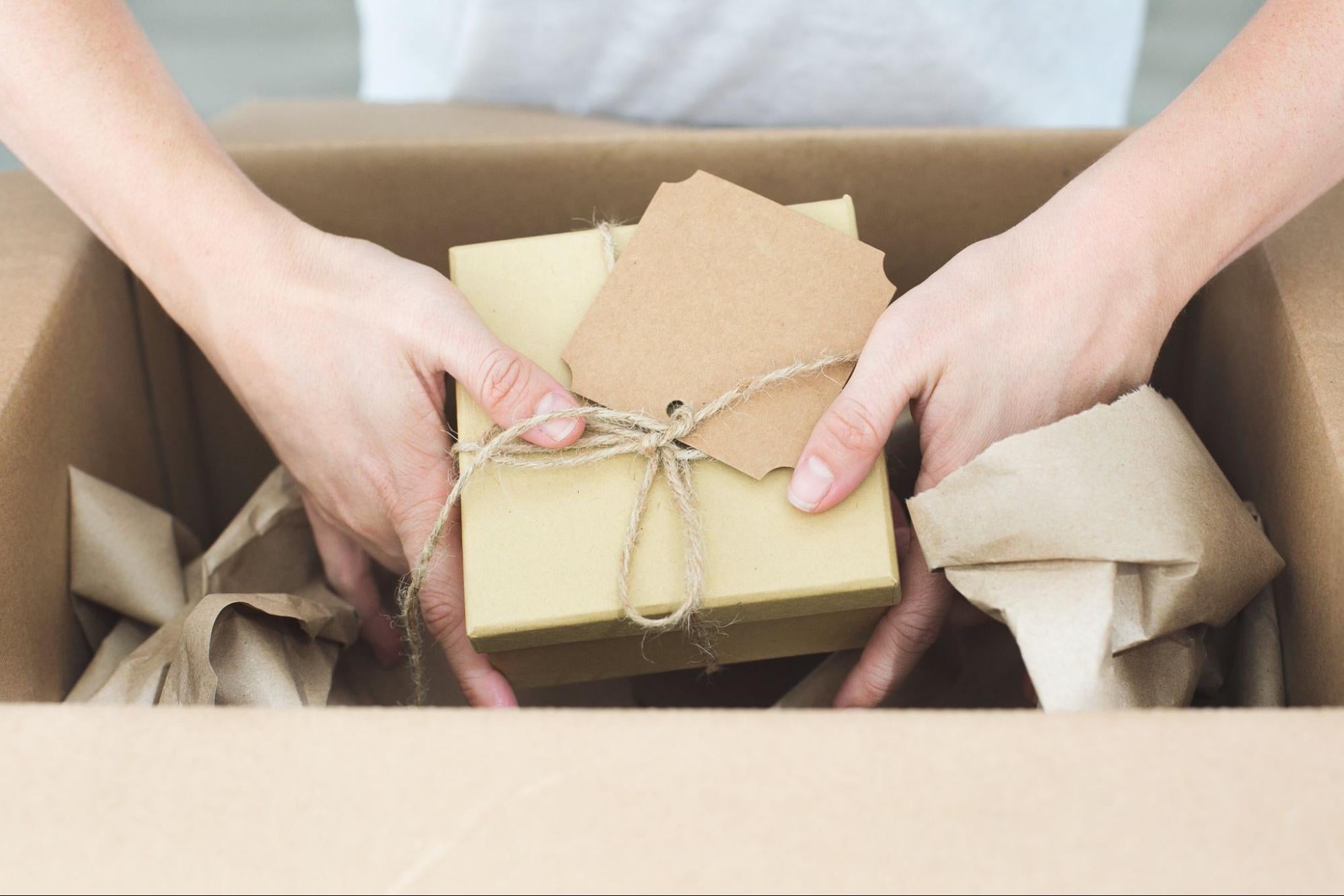 A person lifting a wrapped present from a cardboard box.