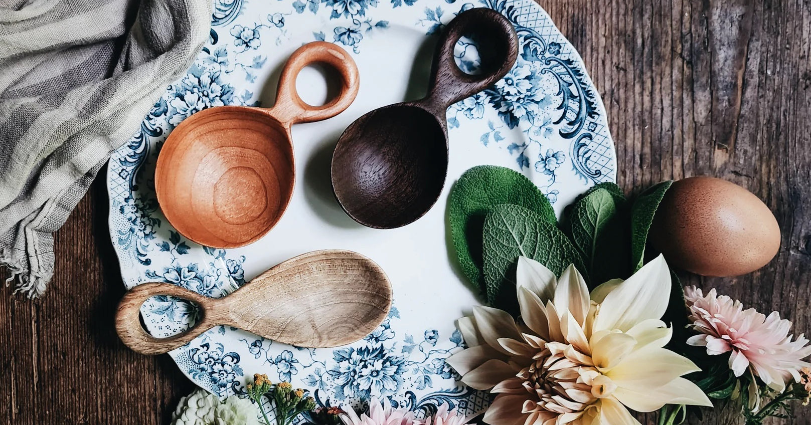 Handmade wooden spoons lay arranged on a table with linens and flowers