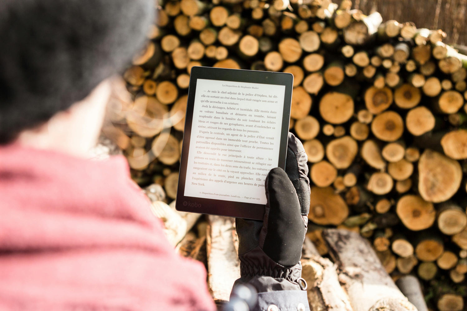 A person reads an ebook in front of a wood pile