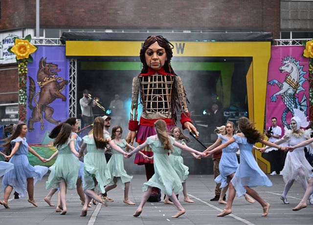 Um die Puppe tanzen (17.5.2024) Menschen in Belfast tanzen um Little Amal, eine mehr als dreieinhalb Meter große Puppe, die vor Krieg, Gewalt und Verfolgung fliehende Kinder symbolisieren soll. Sie steht im Mittelpunkt des Performance-Kunstprojekts »The Walk«, das als Symbol für Menschenrechte und Hoffnung gilt. Drei Puppenspieler sind nötig, damit Amal sich bewegen kann. Sie hat bereits mehr als 150 Städte bereist und ist vier Tage in Nordirlands Hauptstadt zu sehen, bevor sie nach Londonderry weiterreist.