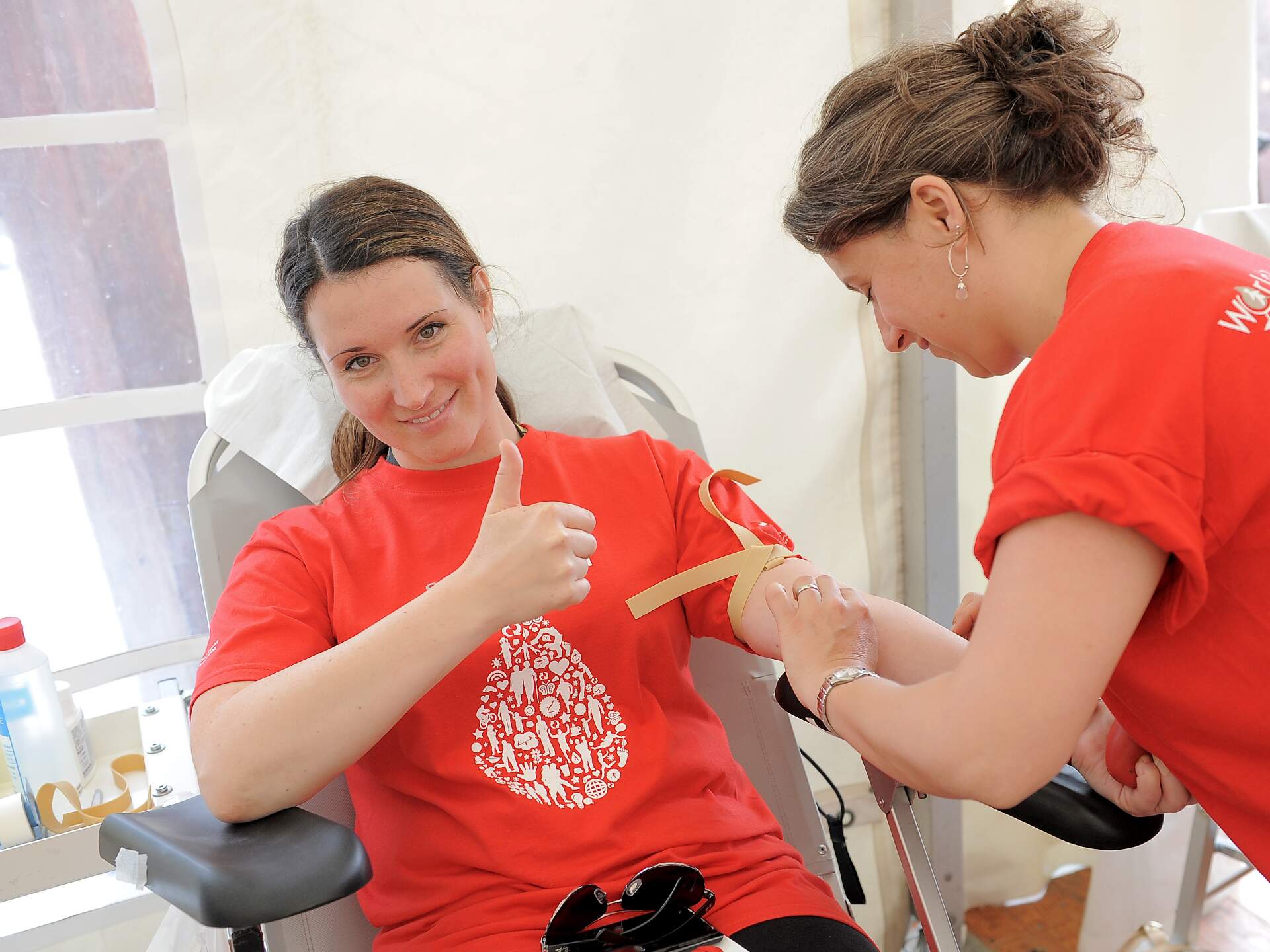 A woman is donating blood and giving a thumbs up whilst smiling