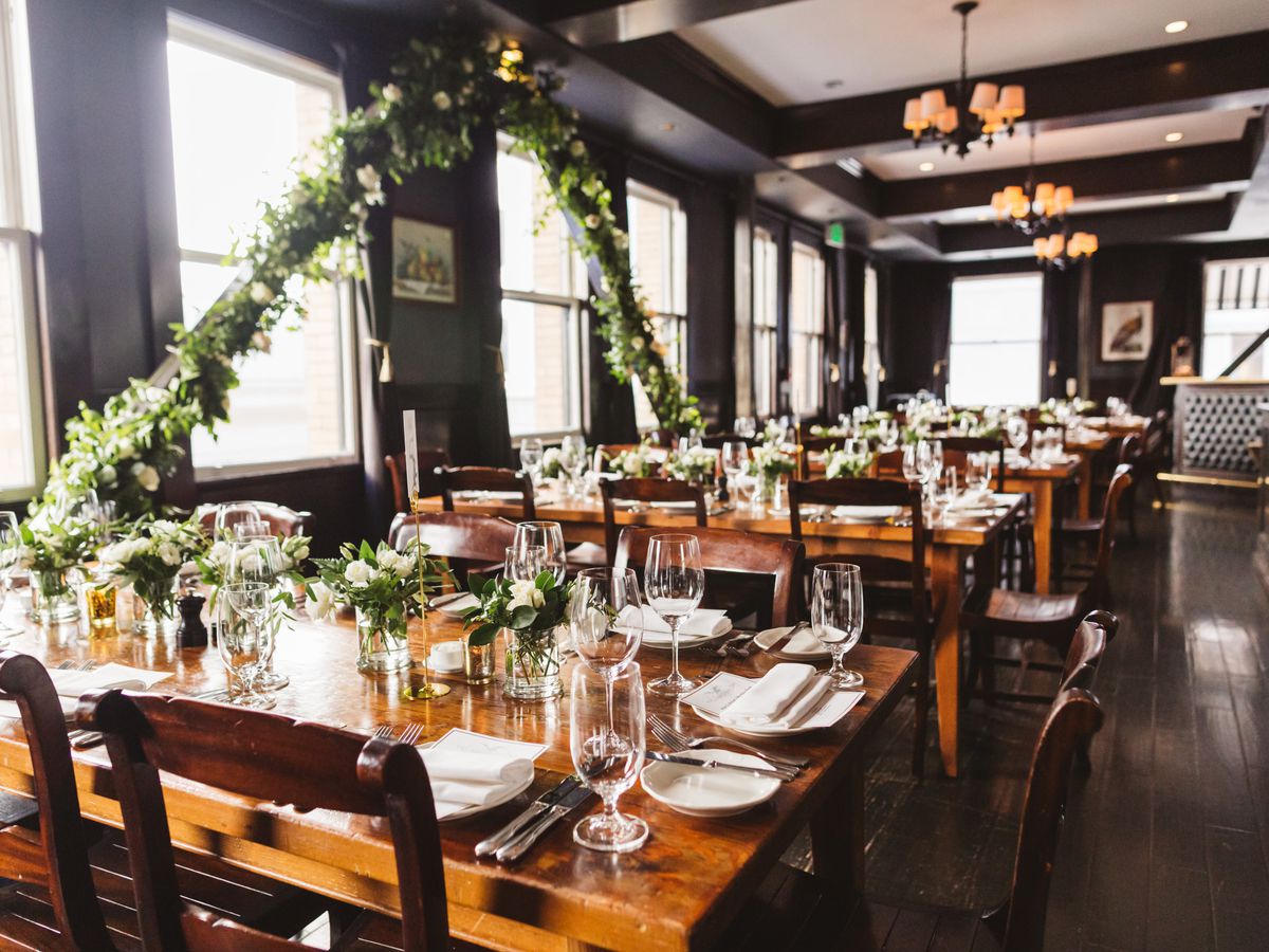 Rows of tables at Wayfare Tavern are decorated with place settings and white flowers for a wedding reception