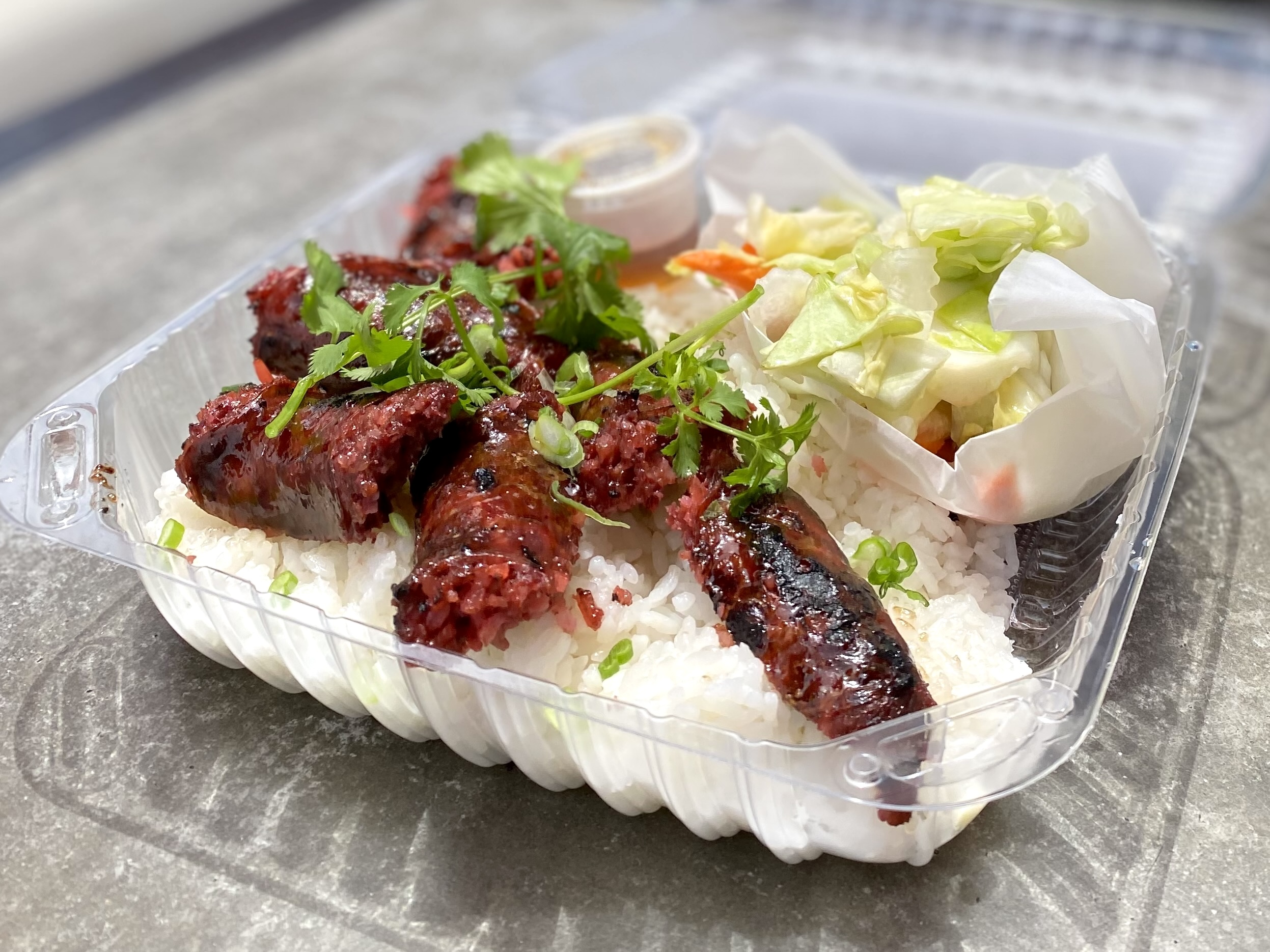 A plastic container filled with rice and sausages with pickled vegetables.