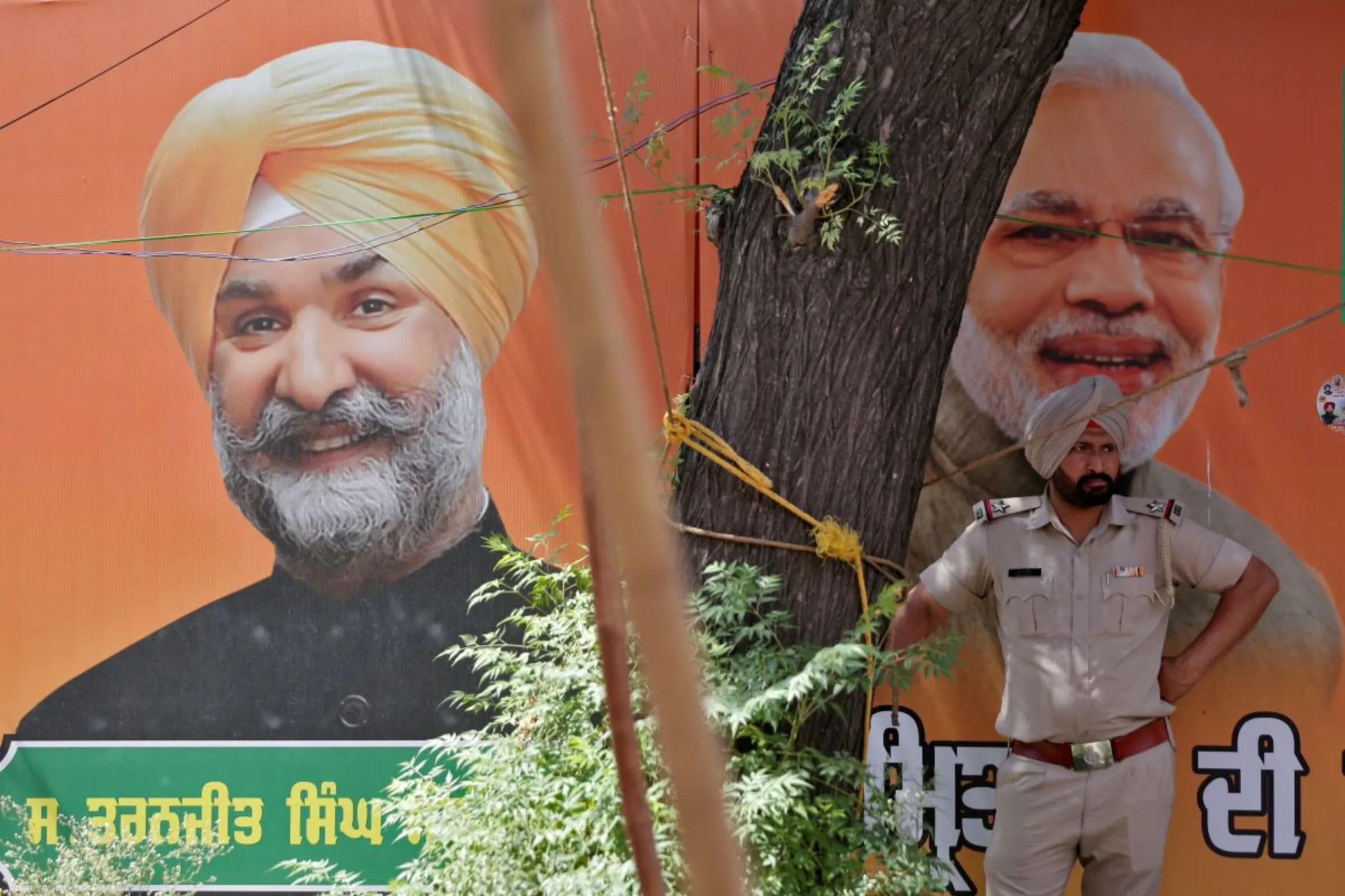A police officer stands in front of a hoarding featuring India's Prime Minister Narendra Modi and Taranjit Singh Sandhu, an election candidate of India's ruling Bharatiya Janata Party (BJP) for Amritsar constituency, before a farmers' protest in Amritsar, India, May 28, 2024. REUTERS/Stringer