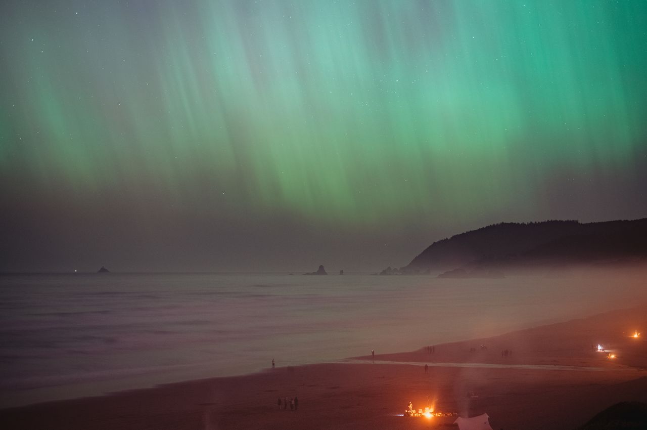 Aurora borealis over the beach with campfires and people.