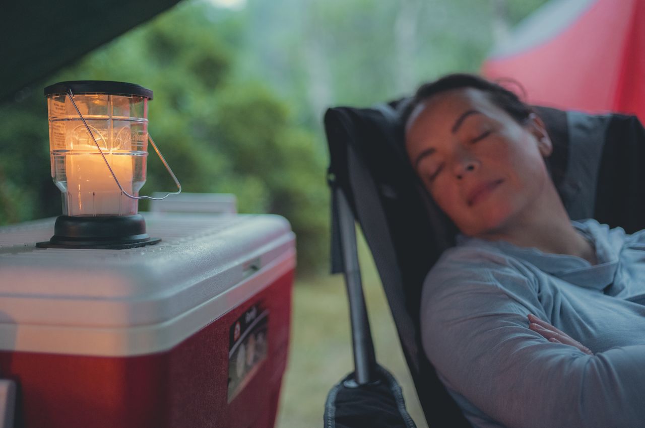 A person sleeping in a camping chair next to a cooler with a candle.